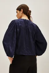 Camisa azul marino de corte holgado con mangas abullonadas, cuello redondo y abertura frontal decorada con tachas metálicas plateadas.