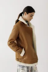 Campera tipo gamulán de cuero color camel con interior y solapas de corderito sintético en color crema. Presenta cierre frontal, bolsillos laterales y detalles de correas ajustables en los puños y la cintura.