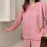 Conjunto de pijama de dos piezas confeccionado en tela de plush texturizada con diseño de rayas verticales en relieve. Incluye una remera de manga larga con cuello redondo y un pantalón de corte holgado. La remera presenta un pequeño bordado decorativo en el pecho.