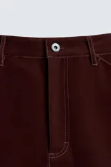 Pantalón de hombre color bordó oscuro, de corte ancho (wide fit), confeccionado en tejido de algodón con acabado flocada o efecto aterciopelado. Presenta cinco bolsillos y cierre frontal con cremallera y botón.