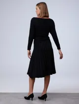 Vestido negro tejido de largo midi, con escote asimétrico adornado con tachas doradas, corte a la cintura y falda plisada. Marca Emma & Michele.