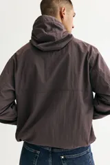 Campera rompevientos de nylon repelente al agua, color gris oscuro/marrón topo, con forro de malla. Presenta cierre frontal con protección para el mentón, capucha ajustable con cordón, bolsillos laterales y bolsillo interior con cierre, y elástico revestido en puños y bajo.