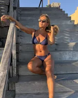 Bikini azul oscuro con tela texturada. El corpiño es triangular con una argolla de zamak en el centro y tirantes finos. La bombacha es colaless con argollas metálicas en los laterales.