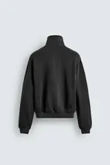 Sudadera de corte relajado confeccionada en algodón con interior de rizo, color amarillo mostaza con efecto lavado. Presenta cuello subido con cierre frontal de cremallera y detalle de cinta trenzada en el tirador, manga larga y acabados en rib.