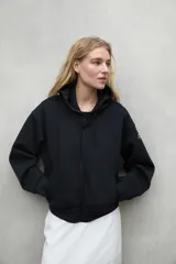 Campera tipo hoodie con cierre frontal, confeccionada en tejido sostenible con capucha ajustable mediante cordones. Presenta mangas largas, puños acanalados y dos bolsillos delanteros.
