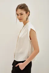 Camisa de corte oversize color negro, con cuello mao, mangas cortas y botones ocultos. Presenta un pin metálico decorativo con strass en el cuello.