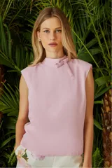Blusa color rosa pálido sin mangas, con cuello alto y lazo decorativo.