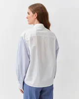 Camisa de algodón con diseño combinado. El cuerpo es de color blanco liso, mientras que las mangas largas y el bolsillo frontal aplicado presentan un patrón de rayas finas celestes y blancas. Cuenta con cuello clásico y cierre frontal de botones.