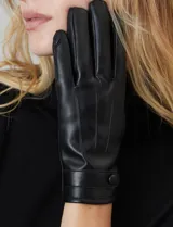 Guantes de cuero sintético color negro, con costuras decorativas en el dorso y detalle de tira con broche a presión en la muñeca. Interior forrado en terciopelo.