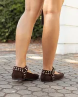 Chatitas de gamuza color chocolate con tira ajustable al tobillo, decorada con remaches metálicos y hebilla plateada.