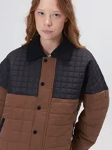 Campera acolchada con diseño de bloques de color en tonos terracota y beige. Presenta cuello camisero y puños en pana negra, cierre frontal oculto con botones a presión y costuras capitoneadas en toda la prenda.