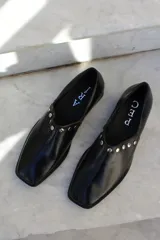 Zapato de cuero vacuno color bordó, con diseño de punta cuadrada y detalle de tachas metálicas planas en el borde superior. Presenta un taco geométrico bajo y costura central en el empeine.