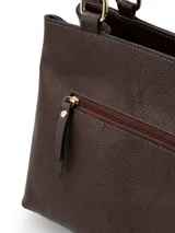Cartera de hombro color chocolate, confeccionada en cuero con textura granulada. Presenta un diseño estructurado con doble asa, herrajes metálicos dorados y un detalle decorativo de nudo con cordones en tono rosado claro en uno de los laterales. Incluye logo metálico de la marca en la parte frontal inferior.
