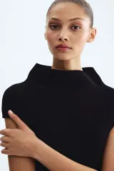 Top en punto suave, de color negro, corte ceñido al cuerpo, cuello alto y mangas cortas con aberturas en los hombros.