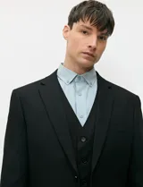 Ambo negro de corte clásico para hombre, compuesto por saco de solapas de muesca con dos botones, chaleco abotonado a juego y pantalón de vestir de corte recto.