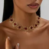 Collar tipo gargantilla de metal dorado con eslabones en forma de flores caladas, cada una con un centro de piedra roja facetada.