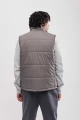 Chaleco puffer color gris topo, con cuello alto y cierre frontal.