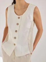 Chaleco sin mangas de lino, con diseño de paneles en color blanco crudo y beige. Presenta escote redondo y cierre frontal con botones de madera marrones.