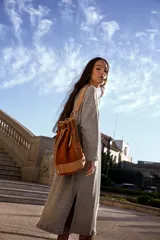 Mochila tipo bucket color marrón tostado, confeccionada en gamuza con detalles en cuero color beige. Cuenta con bolsillo exterior con cierre, bolsillo interior con cierre, llavero interno, asa de mano y correa extraíble y regulable para usar como mochila o bolso de hombro.