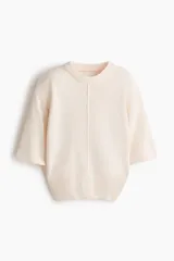 Top de punto color beige, con costura central enlazada al frente, mangas cortas con hombros caídos y ribete acanalado en el cuello, mangas y bajo.