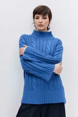 Sweater de punto con diseño de trenzas, cuello alto y mangas largas con puños acampanados. Presenta un corte holgado con terminación asimétrica en el ruedo.