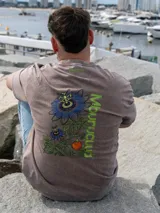 Remera Brixton oversize de algodón, color marrón con efecto acid wash, manga corta y estampa en la espalda de flores de mburucuyá con el texto vertical en color verde.