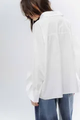 Camisa clásica de algodón con cuello camisero, cierre frontal de botones y mangas largas con puños anchos. Presenta un corte holgado y diseño minimalista.