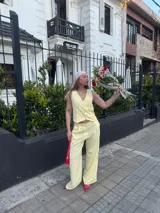 Conjunto de dos piezas compuesto por un chaleco abotonado y un pantalón de corte recto y tiro alto, confeccionado en tela crepé color amarillo pastel.