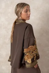 Chaqueta corta estilo kimono color chocolate, con bordados florales en tono dorado en el frente y las mangas. Presenta guardas decorativas bordadas a lo largo del cuello, la apertura frontal y los puños.
