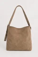 Cartera tipo shopper color marrón de gamuza sintética, con asa larga decorada con ojalillos metálicos plateados y extremos colgantes.