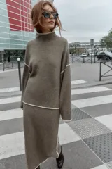 Jersey de punto con cuello subido y manga larga, de corte holgado. Presenta detalles de vivos en color crema en el cuello, puños y costuras de las mangas, contrastando con el tono marrón jaspeado de la prenda.