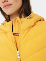 Campera amarilla acolchada con capucha, cierre frontal con cremallera, bolsillos laterales y logo de Tommy Hilfiger en el pecho.