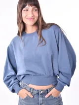 Buzo de tejido de punto color azul piedra, con cuello redondo y costuras verticales en el frente. Presenta un calce holgado con mangas amplias y puños y cintura ajustados con elástico.