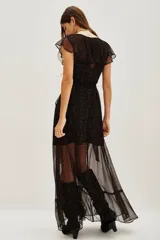 Vestido largo de gasa negra con estampado de puntos dorados, diseño cruzado con volados en el escote y falda, y forro interior corto.