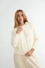 Buzo de tejido de punto color beige, con cuello alto y cierre frontal parcial, de manga larga con puños acanalados y ruedo también acanalado.