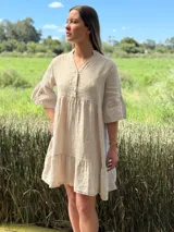 Vestido corto de lino color beige claro, con cuello mao, escote con botones de nácar, mangas tres cuartos con volados y ruedo con volado.