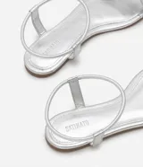 Sandalias planas blancas con tira elástica en el tobillo y tira fija sobre los dedos.