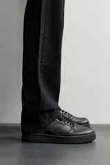 Zapatillas deportivas de estilo retro, color negro, con diseño superior de paneles combinados, cordones al tono y suela gruesa con volumen.