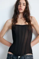 Top corsetero semitransparente con escote palabra de honor, detalle de varillas interiores y bajo asimétrico. Cuenta con cierre lateral con cremallera oculta.
