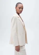 Chaqueta de corte recto y diseño minimalista en color crema, con cuello de solapa, cierre frontal de doble botonadura y forro interior.