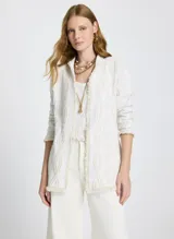 Saco largo tejido color blanco con textura en relieve, corte recto, cuello semi alto, mangas largas y ribete de flecos en el dobladillo, los puños y el cuello.