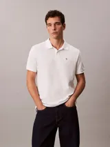 Chomba blanca de piqué de algodón, corte clásico, cuello tradicional, cartera de botones y bajo con aberturas laterales. Tiene un logo bordado en el pecho.