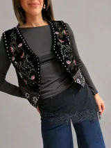 Chaleco de estilo boho chic confeccionado en tela aterciopelada negra, con bordados florales multicolor y detalles de tachas metálicas a lo largo de los bordes frontales.