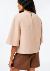 Blusa de manga corta color beige, con cuello redondo y diseño holgado.