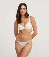 Bombacha colaless de encaje floral color blanco, con tiras laterales finas y ajustables, y detalle de moño pequeño en el frente.