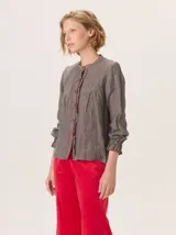 Camisa de algodón color marrón oscuro, con cuello mao, cierre frontal con botones y detalle de volados en la tapeta. Presenta mangas largas con puños elásticos y diseño fluido.