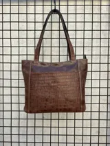 Cartera tipo tote de cuero vacuno negro con doble asa de hombro, panel superior liso y bolsillo exterior frontal con textura símil cocodrilo y costuras visibles en contraste.