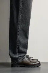 Zapato de cordones de estilo derby, color negro, con parte superior lisa, detalle de bordón en el empeine, horma redonda y suela track dentada.