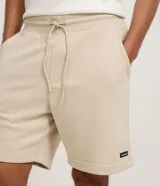 Bermuda masculina de corte slim, confeccionada en tejido de algodón con felpa. Presenta cintura elástica con cordón ajustable, bolsillos laterales y una pequeña etiqueta aplicada en el ruedo.