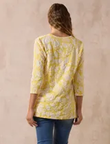 Blusa amarilla estampada con motivos florales en blanco, escote en V y mangas tres cuartos.